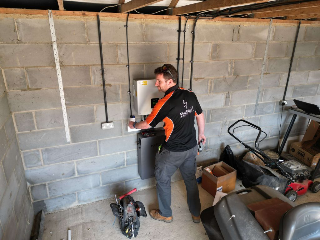 Electric11 engineer inspecting a solar inverter and battery system in a garage