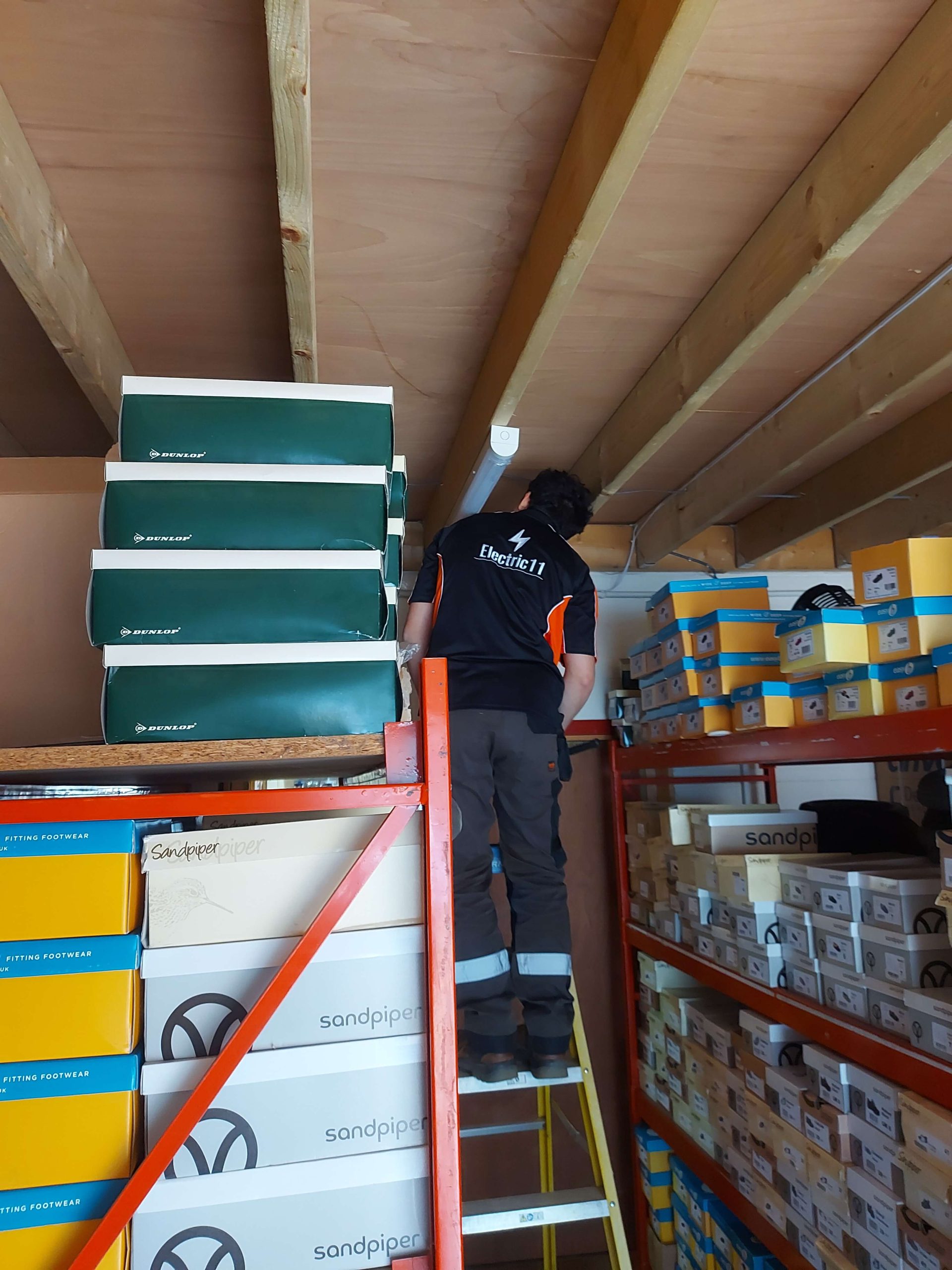 Electrician installing wiring in storage room with shelves of shoe boxes