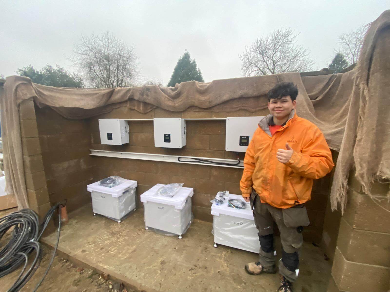 Electrician installing three Fox ESS inverters and battery storage units in an outdoor enclosure.