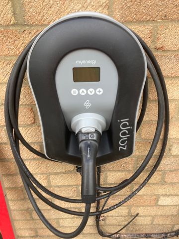 Close-up of a Myenergi Zappi tethered EV charging point mounted on a brick wall.