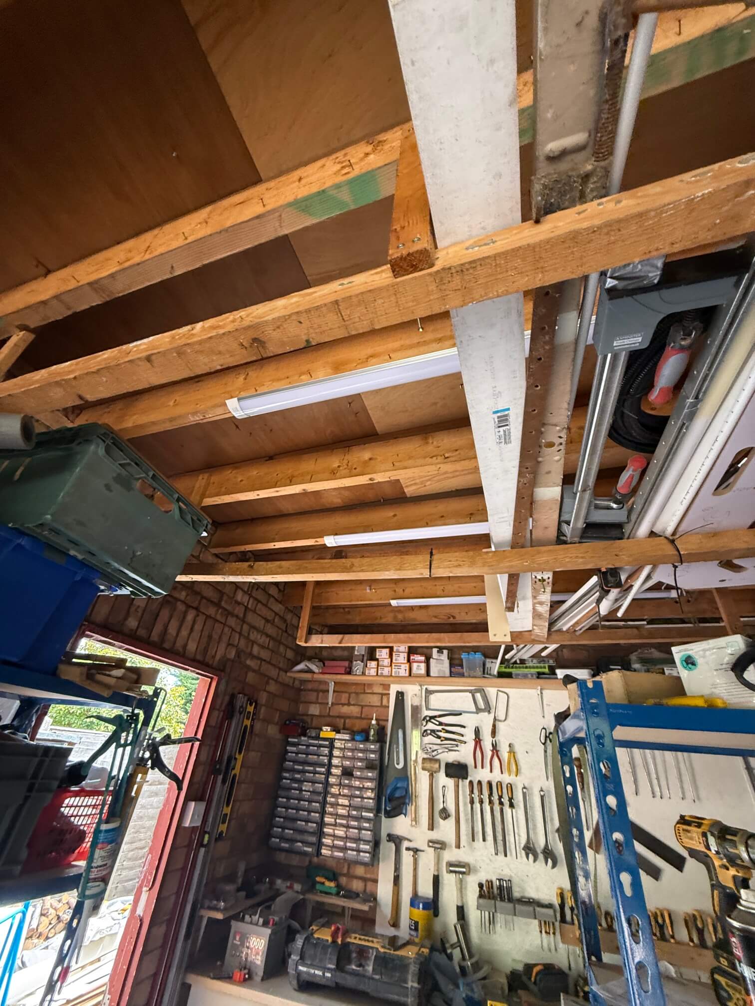 Batten lights mounted beneath exposed garage roof timbers above a tool storage area.