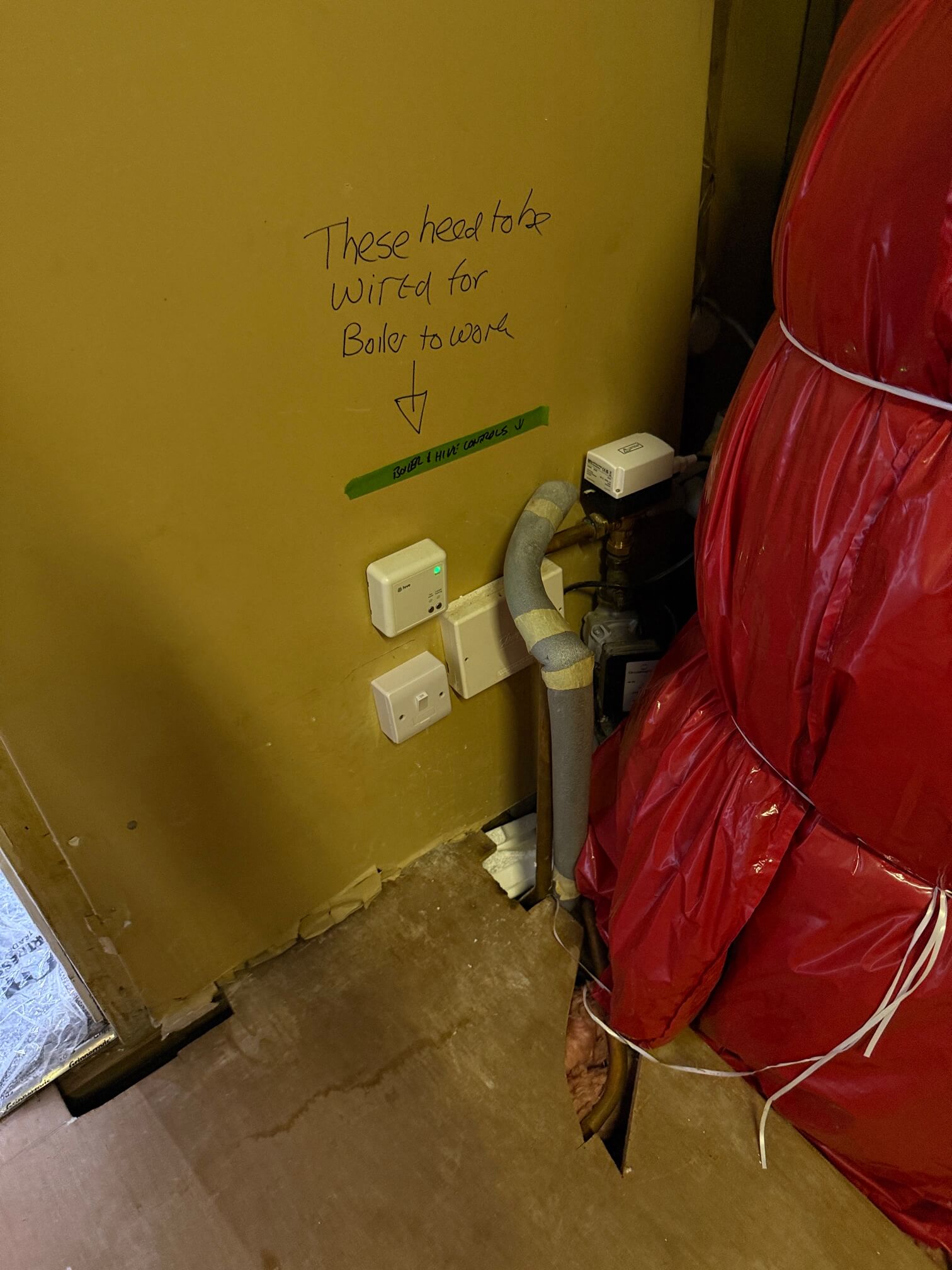 Heating controls and electrical connection plates beside an insulated hot water cylinder.