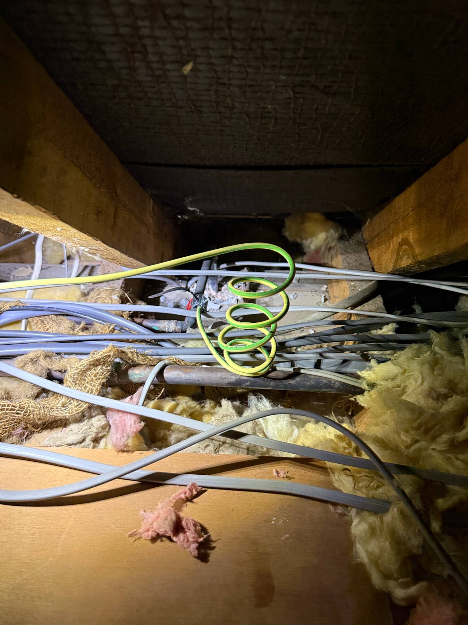 Electrical cables and a coiled green-and-yellow conductor between loft timbers and insulation.
