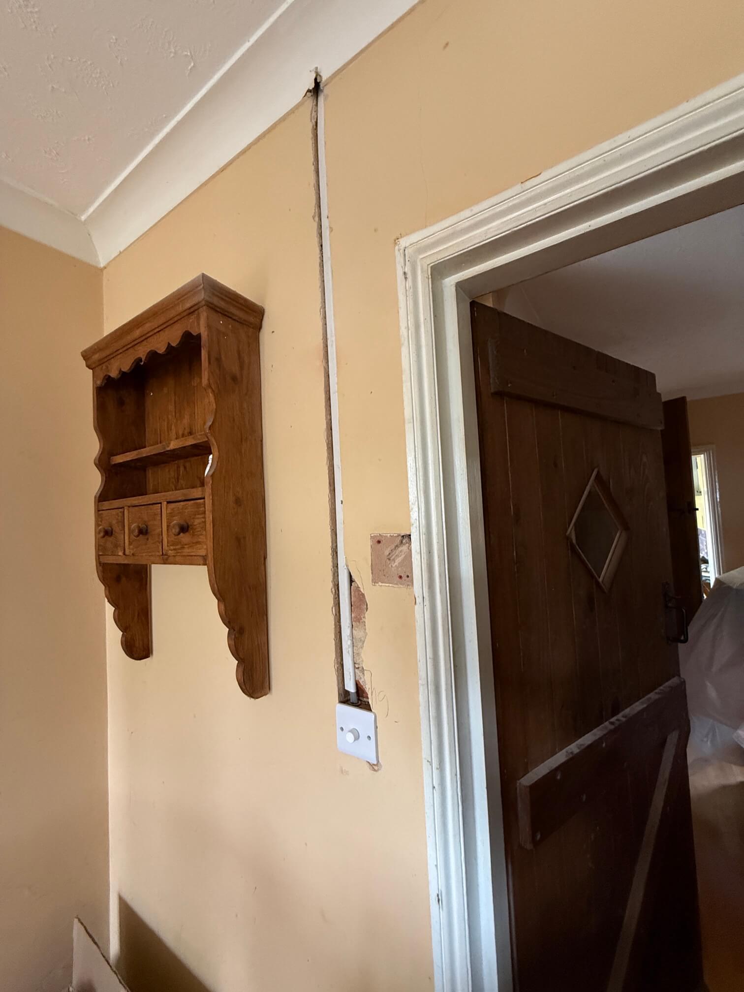 White rotary wall control beneath a vertical cable route beside a wooden door.