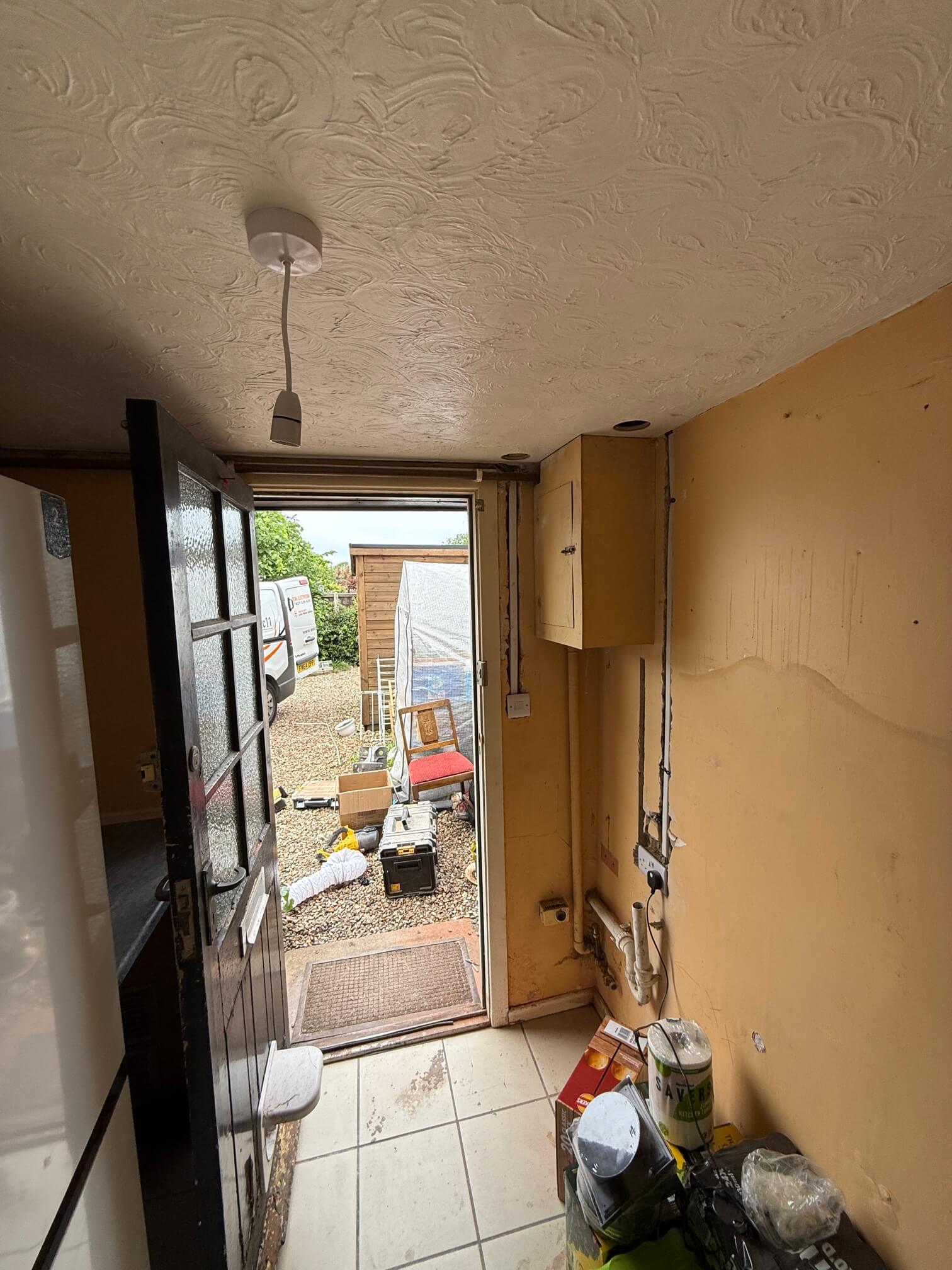 Kitchen wall chases beside a doorway, with a socket, ceiling pendant and tools visible.