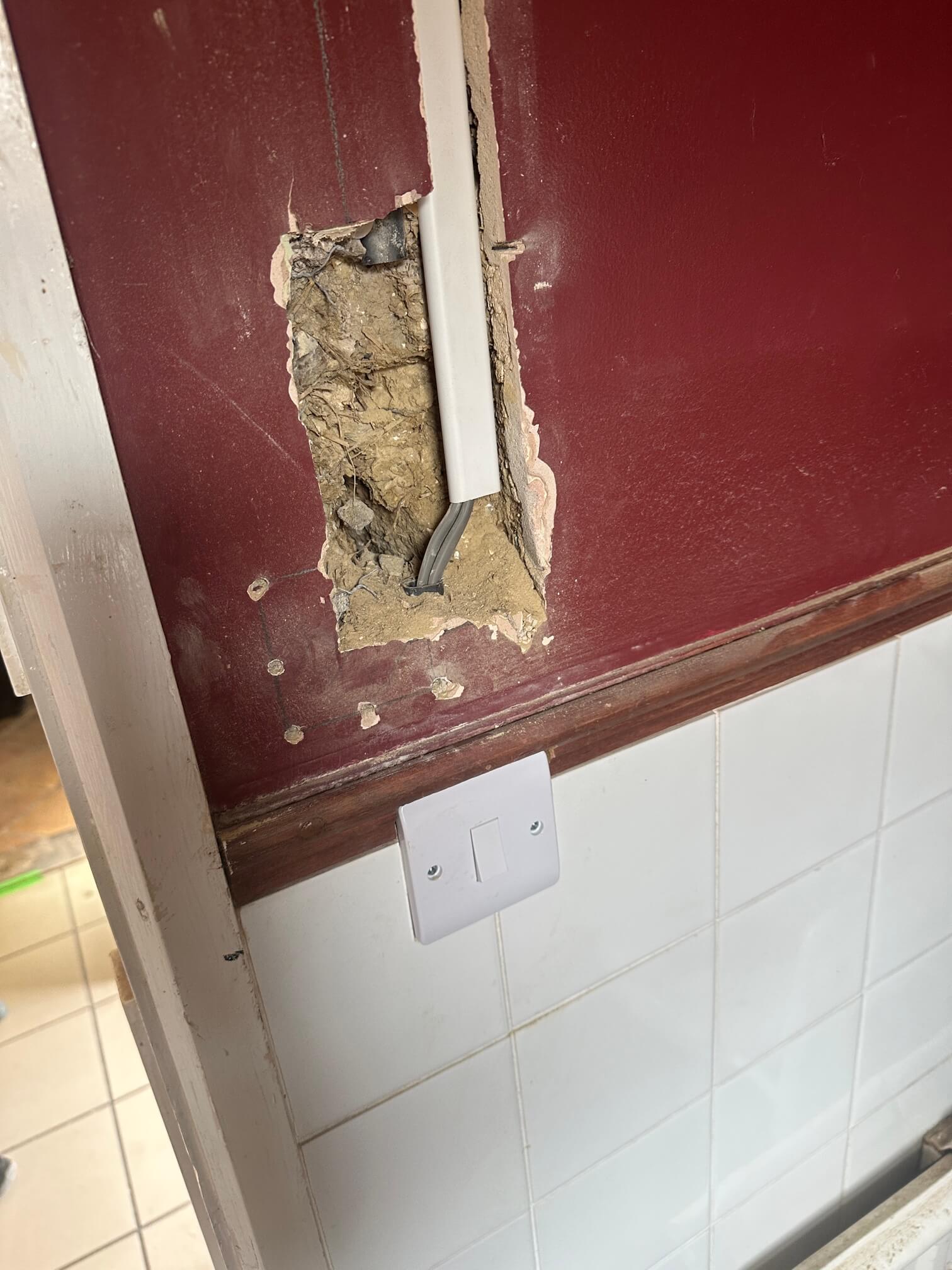 White switch below an exposed cable route on a red wall beside a door frame.