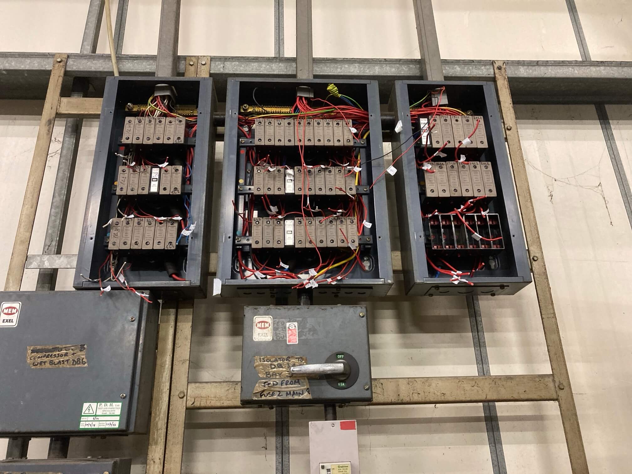 Three open existing fuse boards with labelled conductors and switchgear mounted below.