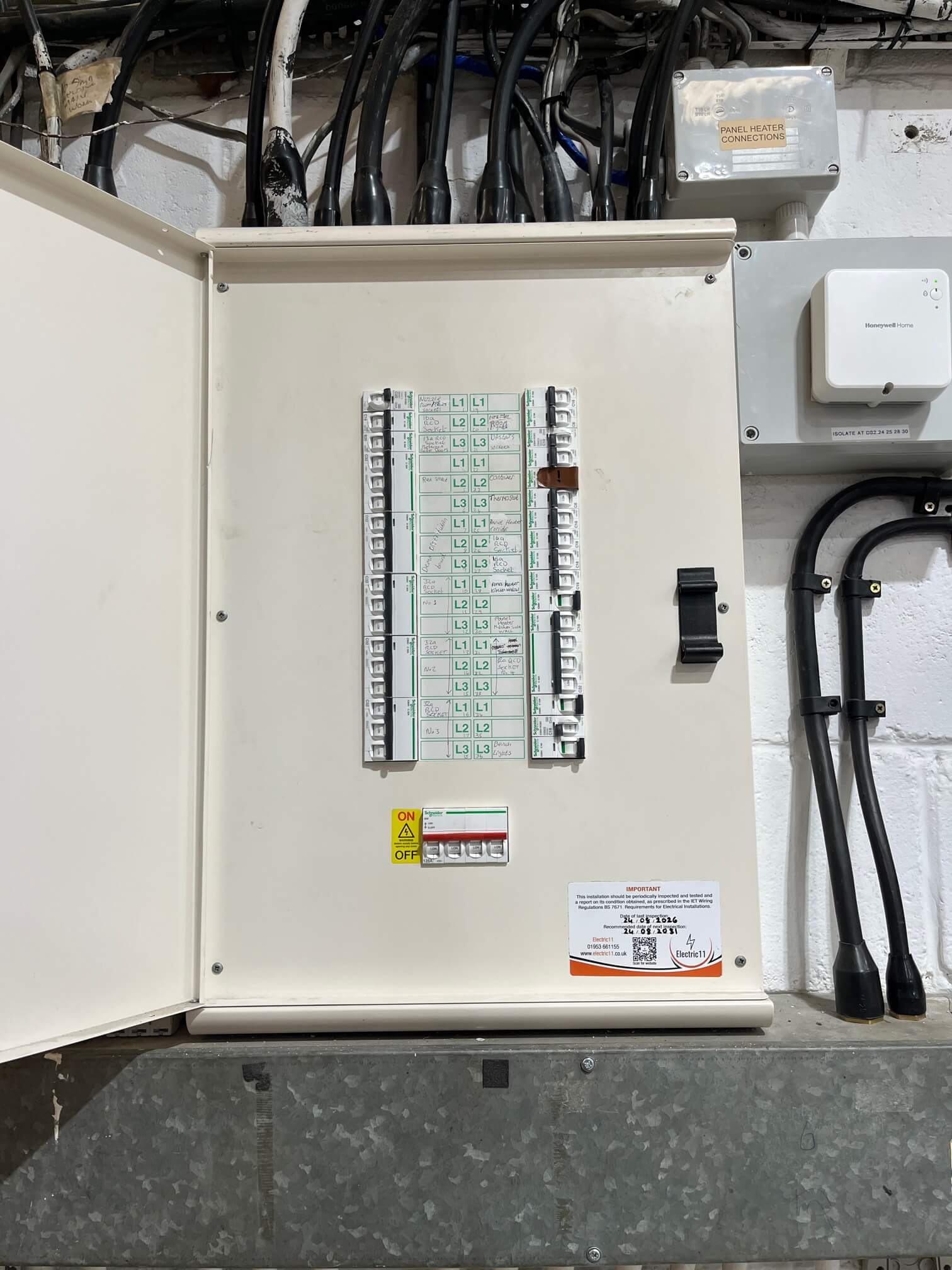 Open distribution board with circuit breakers, handwritten circuit labels and an Electric11 inspection sticker.