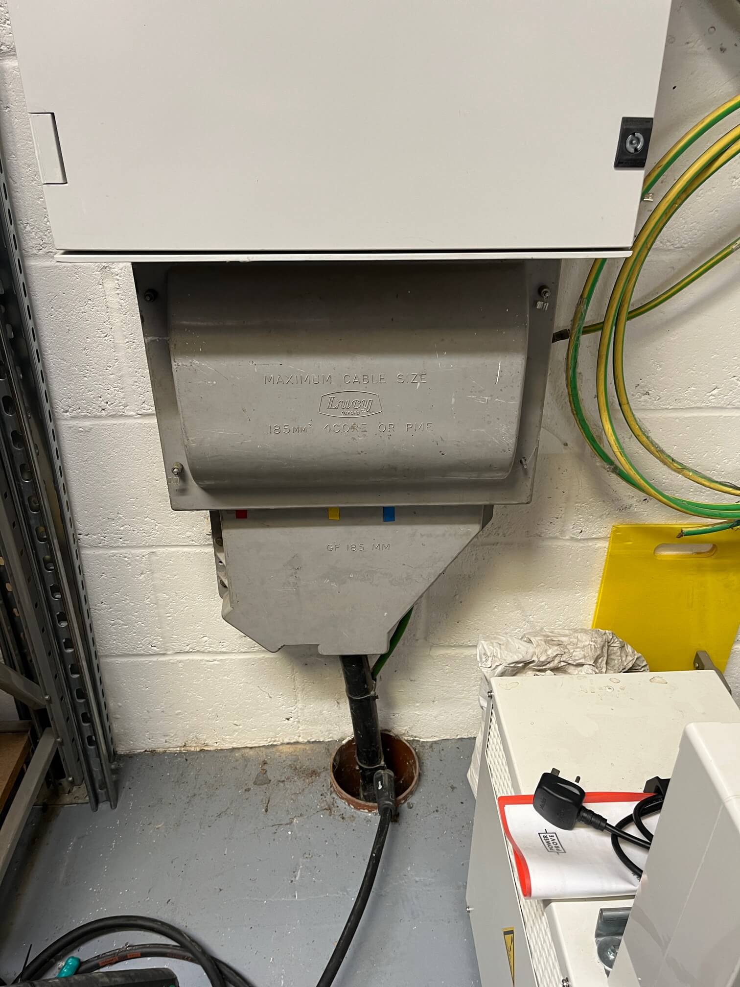 Metal incoming electrical supply enclosure below the meter cabinet with adjacent earthing cables.